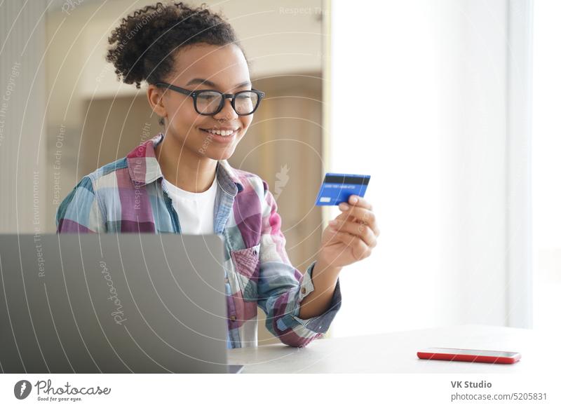 Happy african american young girl holding credit card uses online banking services on laptop at desk online service e commerce money finance store computer