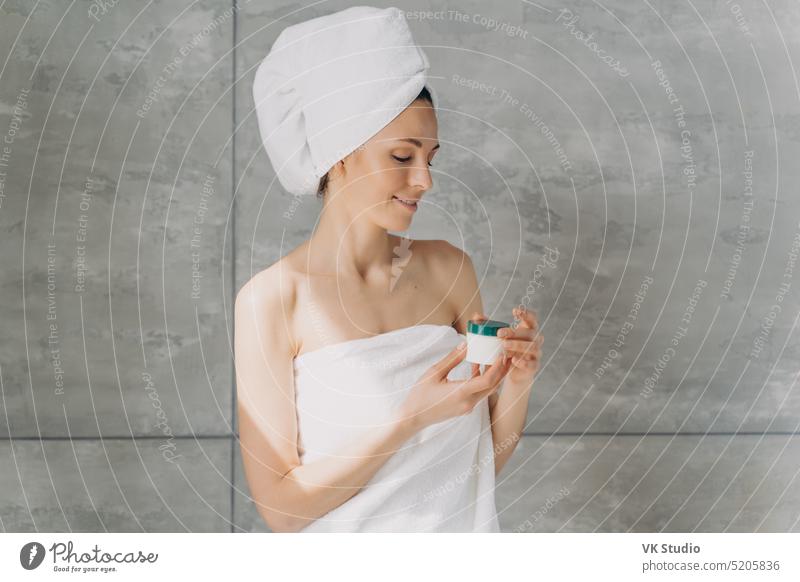 Young girl in towel holds cosmetic jar with cream in bathroom. Skincare beauty products advertising female skincare serum treatment natural mock up woman
