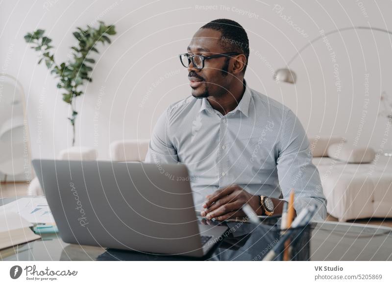 Pensive african american businessman working on laptop thinking over business project, looking aside pensive job ponder office male glasses workplace