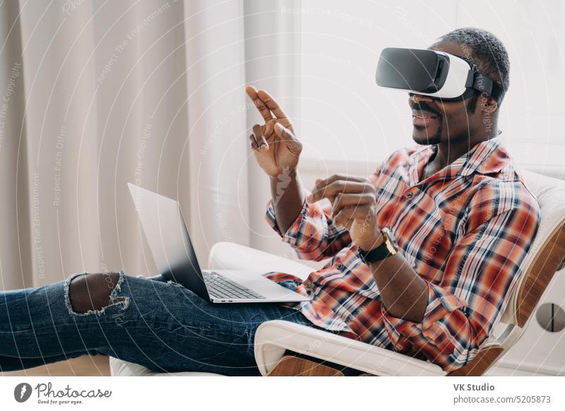 African american man in virtual reality glasses works or play video game on laptop, sitting in chair african american augmented developer software app vr visual