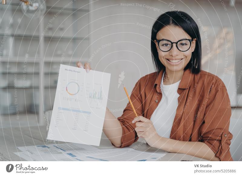 Smiling female financial analyst shows document with company statistics, presents project at desk friendly data startup career sit brunette pretty economist