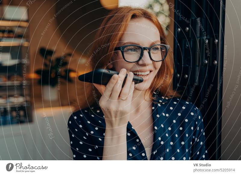Happy smiling businesswoman talks on cell phone on loudspeaker while leaving coffee shop speakerphone smartphone audio record cellphone virtual assistant happy