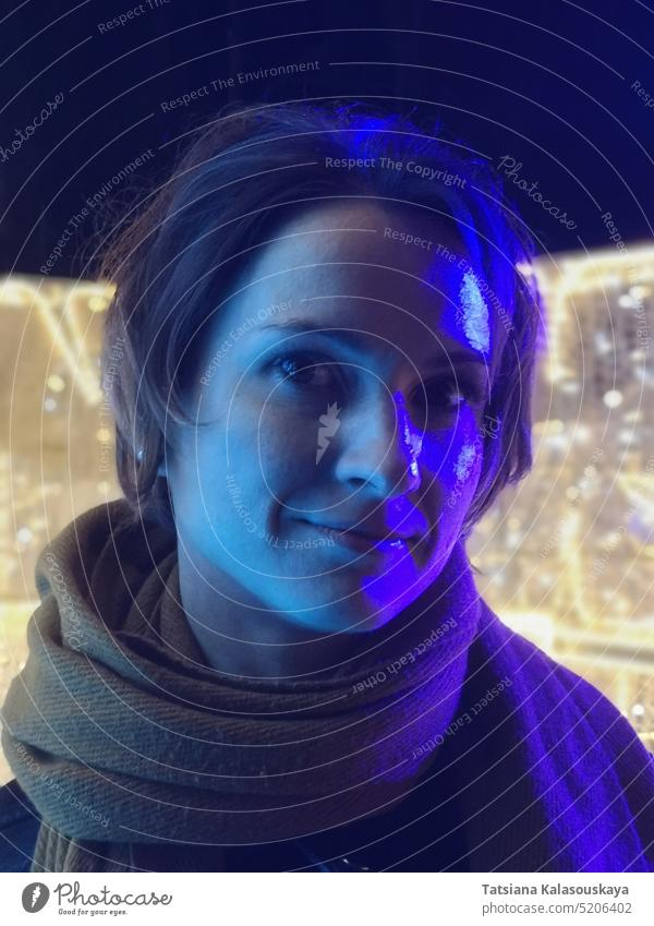 Purple and blue neon light illuminates face of young dark haired woman on yellow lights background Blue Neon Light up Face youthful Dark-haired Woman portrait
