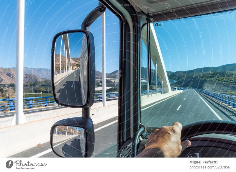 View from the driving position of a truck of the road where it drives when passing over a bridge and of the rear view mirrors reflecting the bridge. driver