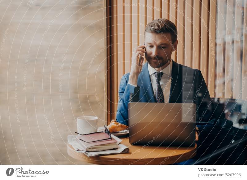 Portrait of elegant finance man in stylish suit sitting in cafe with open laptop young businessman call talk remotely computer focused serious smartphone
