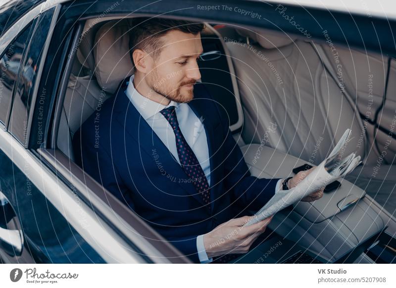 Thoughtful executive manager in formal suit reading newspaper in backseat of limousine thoughtful young bearded dark blue rides work his office business center