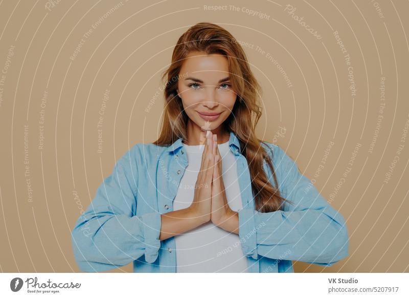 Young woman making namaste gesture isolated on beige background peace meditate luck praying please peaceful hopeful help forgiveness faithful beg ask friendly