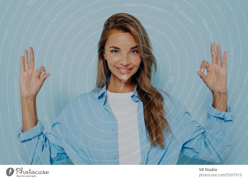 Charming woman making okay gesture against light blue background calmness mudra caucasian fashion face youth long hair friendly beauty fine face expression
