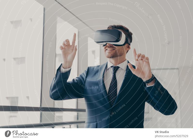 Excited office worker in vr headset or virtual reality goggles gesturing with hands excited amazed impressed smiling touching objects digital world businessman