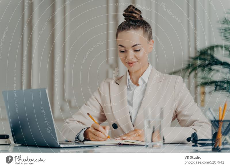 Attracative successful businesswoman in elegant suit making to do list at work computer internet office technology looking manager notebook notepad owner