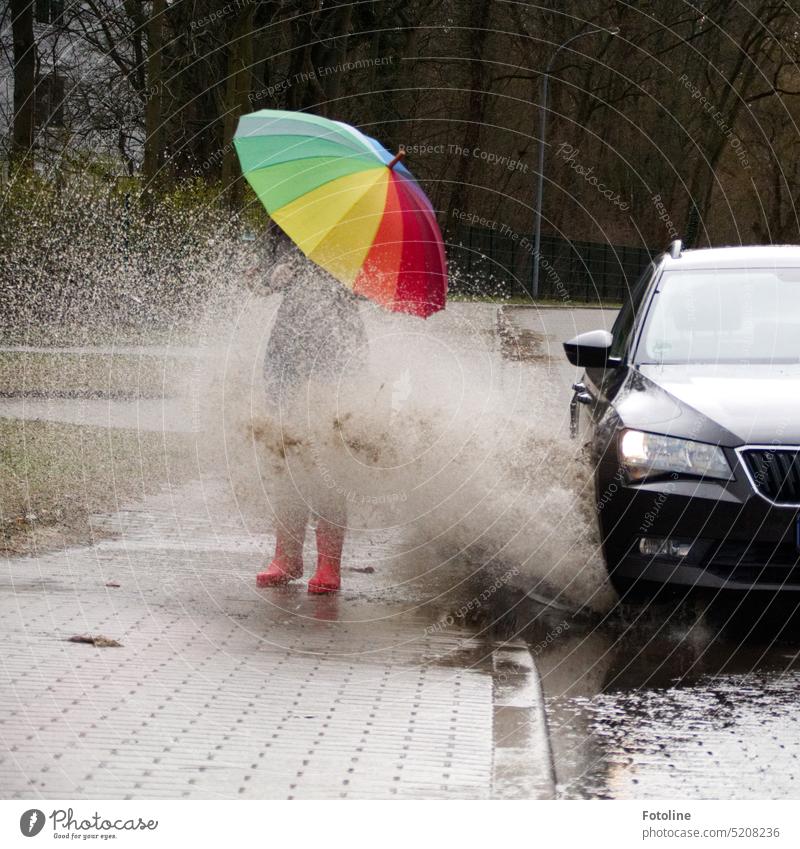 Whoosh!!! There thunders the dark car full through a deep puddle. A huge shower of water drenches the pedestrian with a colorful umbrella and red rubber boots.