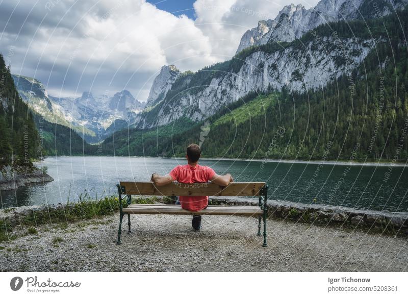 Man relaxing on bench in front of Dachstein Mountains reflected in Gosau lake, Austria austria dachstein gosau male mountains nature landscape travel alps water
