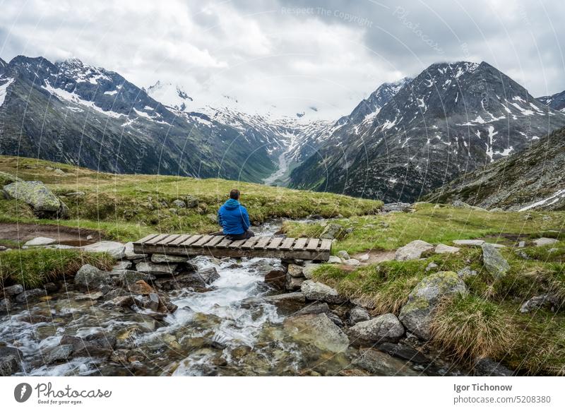 Man hiker resting on small bridge over mountaian river at Schlegeis Lake, Zillertal Alps, Austria zillertal schlegeis austria stausee view beautiful lake hiking