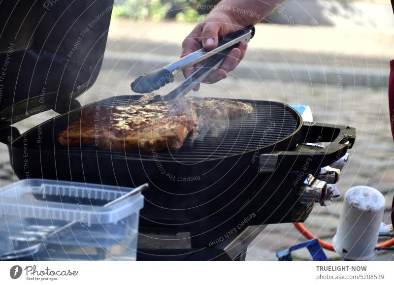 Street food is on the rise - master hand with turning tongs roasting and turning meat on a propane grill outside on the street Barbecue (apparatus) BBQ