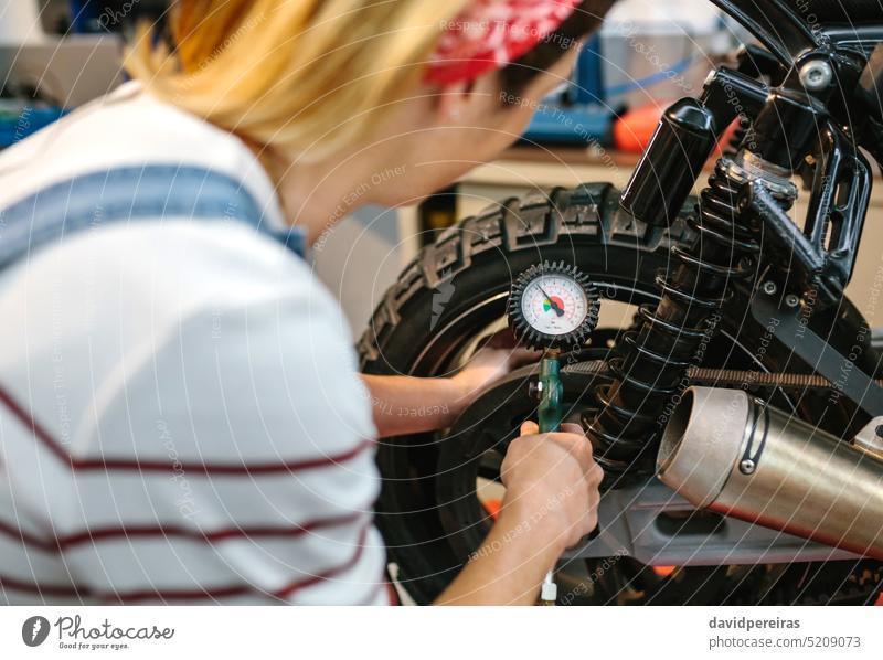 Mechanic woman checking tire air pressure of motorcycle unrecognizable mechanic female tyre wheel motorbike manometer working factory garage worker valve brake