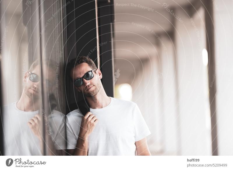 The young man with sunglasses leans casually against a wall and looks thoughtfully into the camera Young man Easygoing Masculinity Nonchalance Manly Face Think