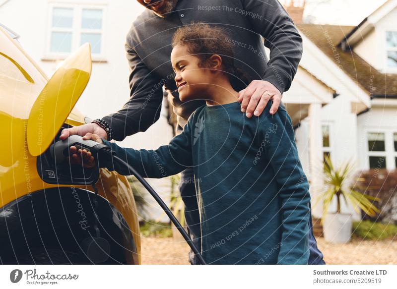 Father helping son with Down syndrome plug electric charger into car boy child father down syndrome multiracial hand hold insert connection control house