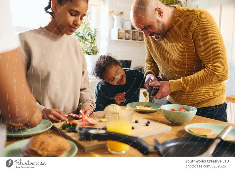 Boy with Down syndrome having pancakes for breakfast with family boy down syndrome multiracial serve eat pour syrup parent four black kitchen food make fun