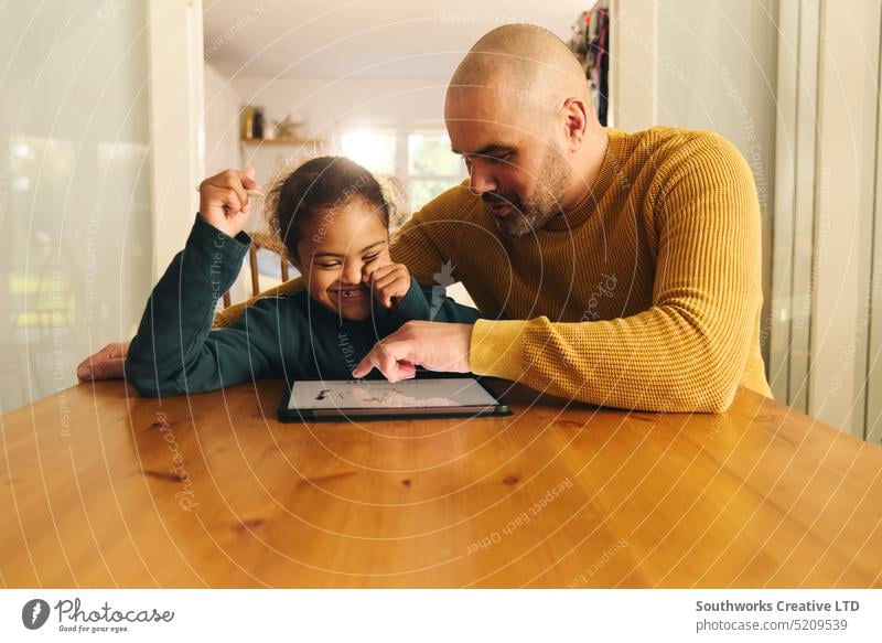 Multiracial father and son with Down syndrome using digital tablet for homework fathers day lifestyle multiracial down syndrome man boy child elementary adult