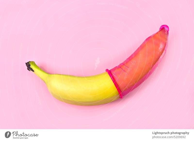 Red condom on banana with pink background. Safe sex concept. symbol sex education sexual issues aids contraceptive erection sex and reproduction protection