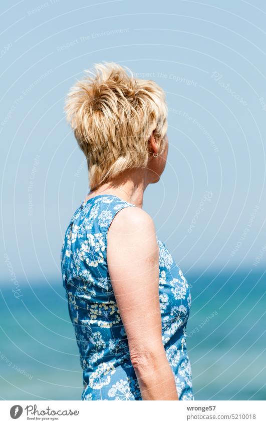 A blonde woman dressed in a blue and white dress looks at the distant sea Summer Sun sunshine blond woman Blonde hair Ocean Baltic Sea Dress blue/white