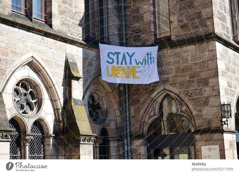 Stay with Ukraine fabric banner on the old facade of the Basilica of Our Lady in autumn sunshine in the old town of Maastricht on the Meuse River in the province of Limburg of the Netherlands