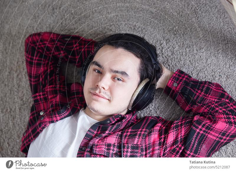Portrait of young man with headphones, smiling happily. guy lying carpet relax music home lifestyle casual people portrait caucasian handsome floor single