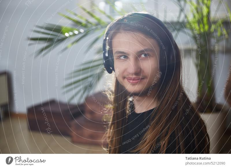 Portrait of a young man with long hair wearing headphones at home student online music listening person male guy internet work white technology caucasian casual