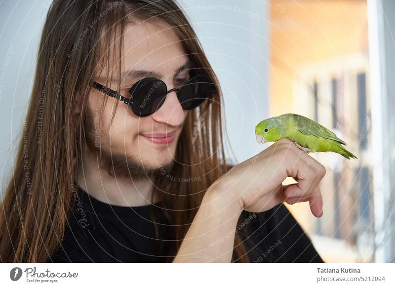 A guy with long hair communicates with a parrot forpus pets parrots exotic beak care yellow feather lifestyle tropical portrait friends hand wing parakeet small