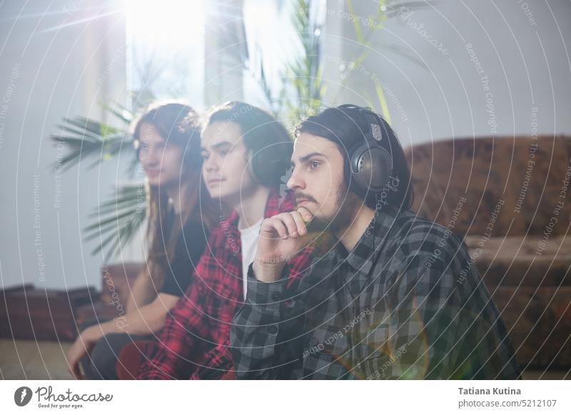 Three men with mobile phones and headphones enjoy music at home. A group of three young people feeling free, enjoying life musicians living room houses