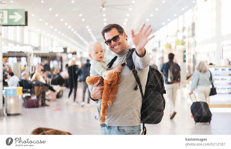 Father traveling with child, holding his infant baby boy at airport terminal waiting to board a plane waving goodby. Travel with kids concept. dad father love