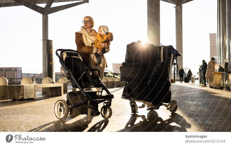 Motherat travelling with his infant baby boy child, walking, pushing baby stroller and luggage cart in front of airport terminal station. vacation trip family
