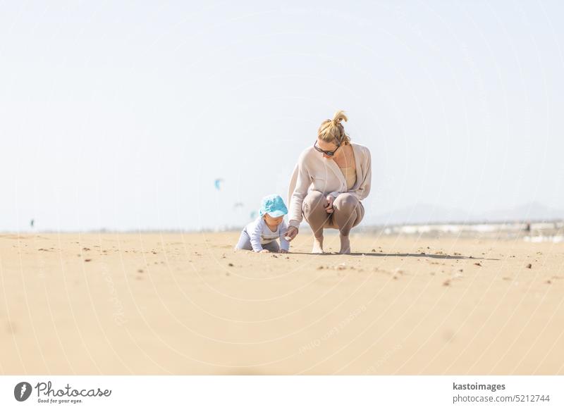Mother playing his infant baby boy son on sandy beach enjoying summer vacationson on Lanzarote island, Spain. Family travel and vacations concept. holidays
