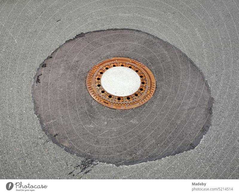 Rusty round manhole cover on repaired grey asphalt in Oerlinghausen near Bielefeld at Hermannsweg in Teutoburg Forest in East Westphalia-Lippe Gully