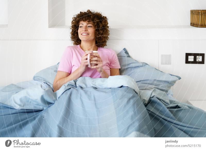 Smiling woman with cup of hot drink on bed enjoy wake up awake coffee lounge morning female smile bedroom weekend lazy relax holiday beverage comfort lady rest