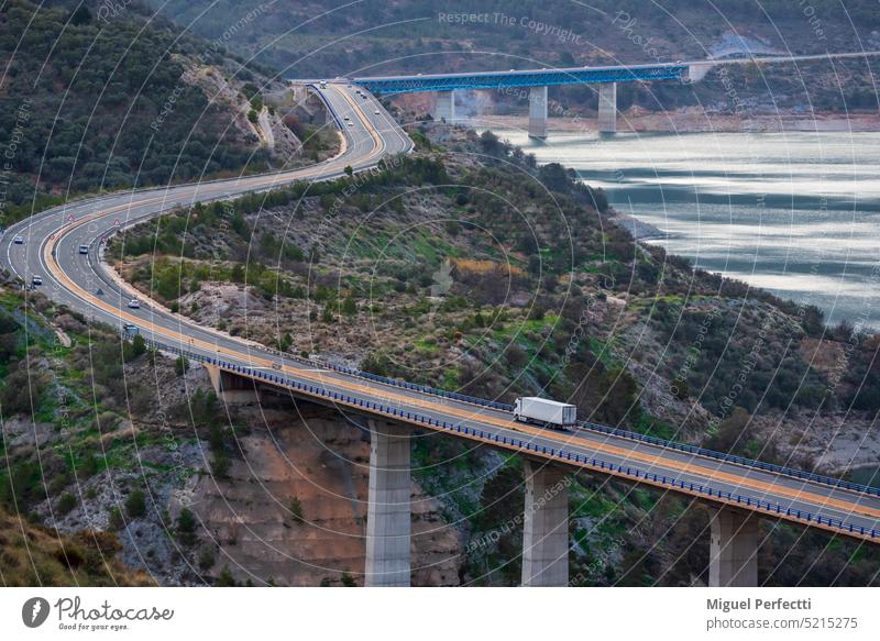Refrigerated truck driving on a highway with bridges over a swamp, road landscape in the mountains and next to a dam. refrigerator motorway viaduct transport