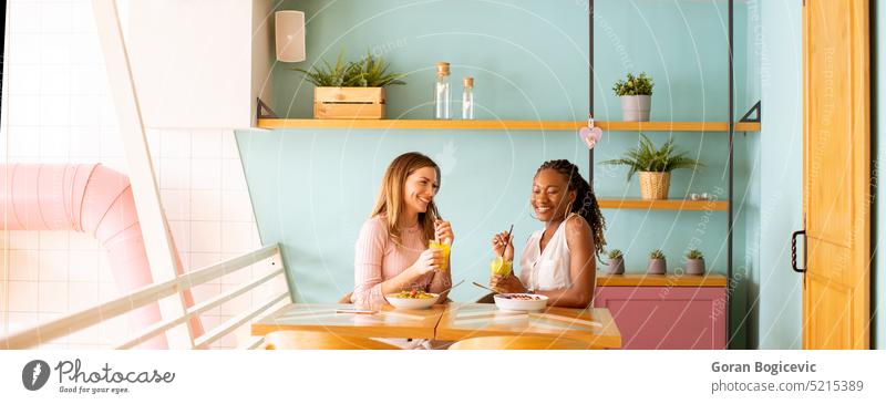 Young black and caucasian woman having good time, drinking fresh juices and having healthy breakfast in the cafe lifestyle ethnicity fruit happy two beautiful