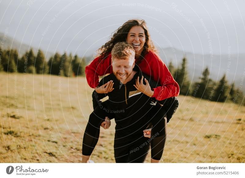 Young woman riding piggyback on a boyfriend at green hills active activity adults adventure backpack caucasian countryside couple curly female field freedom