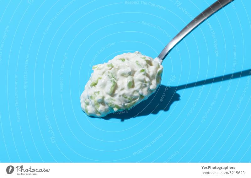 Tzatziki sauce on a spoon, isolated on a blue background above appetizer breakfast bright cacik close-up color copy space cream cucumber cuisine cut out dairy