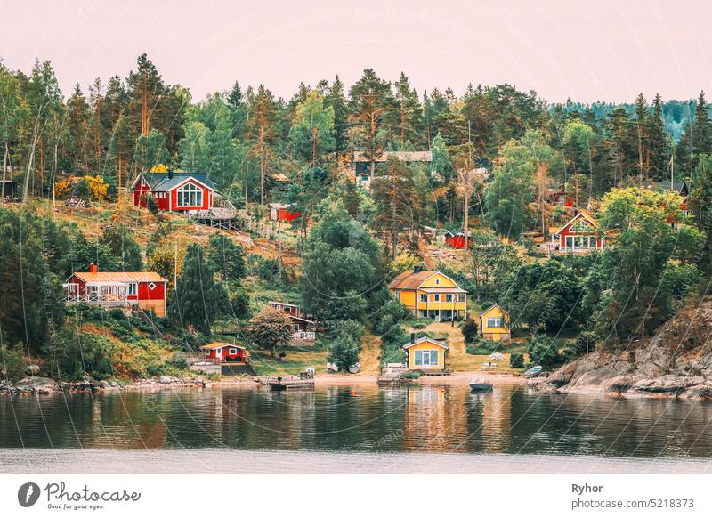 Sweden. Many Beautiful Red And Yellow Swedish Wooden Log Cabins Houses On Rocky Island Coast In Summer Evening. Lake Or River Landscape sweden house huts hygge