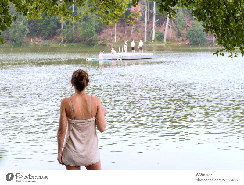 A young woman has bathed in the lake and now watches the other bathers from the shore Woman Lake be afloat free time Weekend holidays vacation recover
