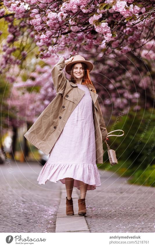 Beautiful young brunette woman with long hair flying in the wind and brown hat in a flowering garden. shallow depth of field. spring day park beautiful girl