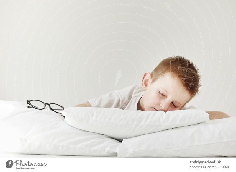 Adorable little boy sleeping in bed. morning dreaming on white bed. glasses from the side child baby pillow bedtime hand person kid face animal innocence