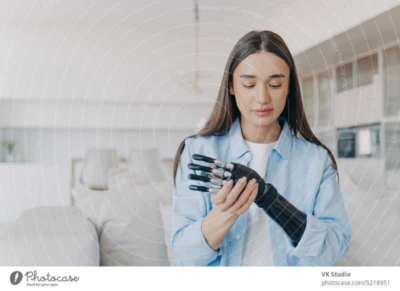 Beautiful young woman learns to install her high tech bionic prosthetic arm, sitting on sofa at home girl disabled prosthesis grasp grip hand artificial limb