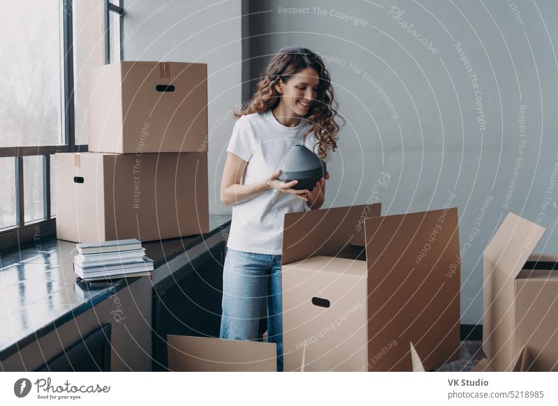 Happy homeowner woman unpack box with belongings at new home on moving day. Mortgage advertising female removal real estate take out package relocation hispanic