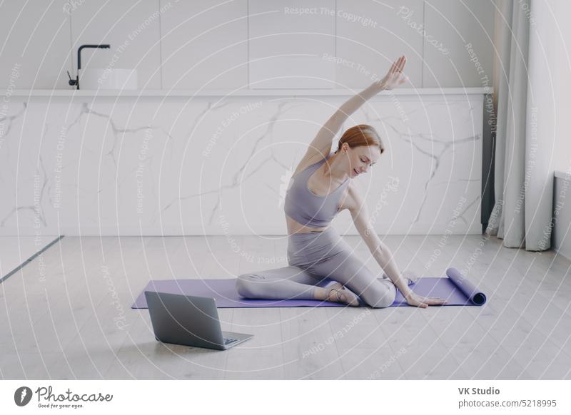 Young woman is stretching and practicing yoga on floor. Sport and healthy lifestyle on quarantine. person laptop computer pilates sport tutorial exercising