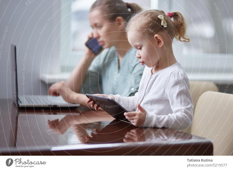 A girl is playing with a tablet. Stressed mother working attending a phone call and taking care of her baby at office child gadget freelancer maternity family