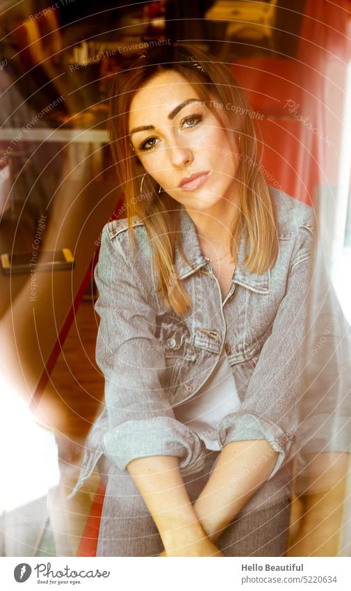 Woman sitting in restaurant, photographed through the window Model Window outlook Jeans jacket Denim Red creoles Jewellery Diner USA America feminine makeup
