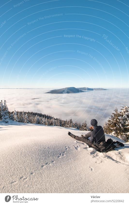 Mountaineer rests on a clearing overlooking the surrounding Beskydy Mountains in the Moravian-Silesian region after climbing Lysa Hora. Enjoying breakfast above the clouds at sunrise
