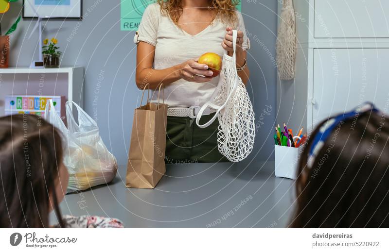 Unrecognizable teacher putting apple in reusable hopping bag in ecology classroom unrecognizable female woman holding reusable bag eco bag fruits plastic free